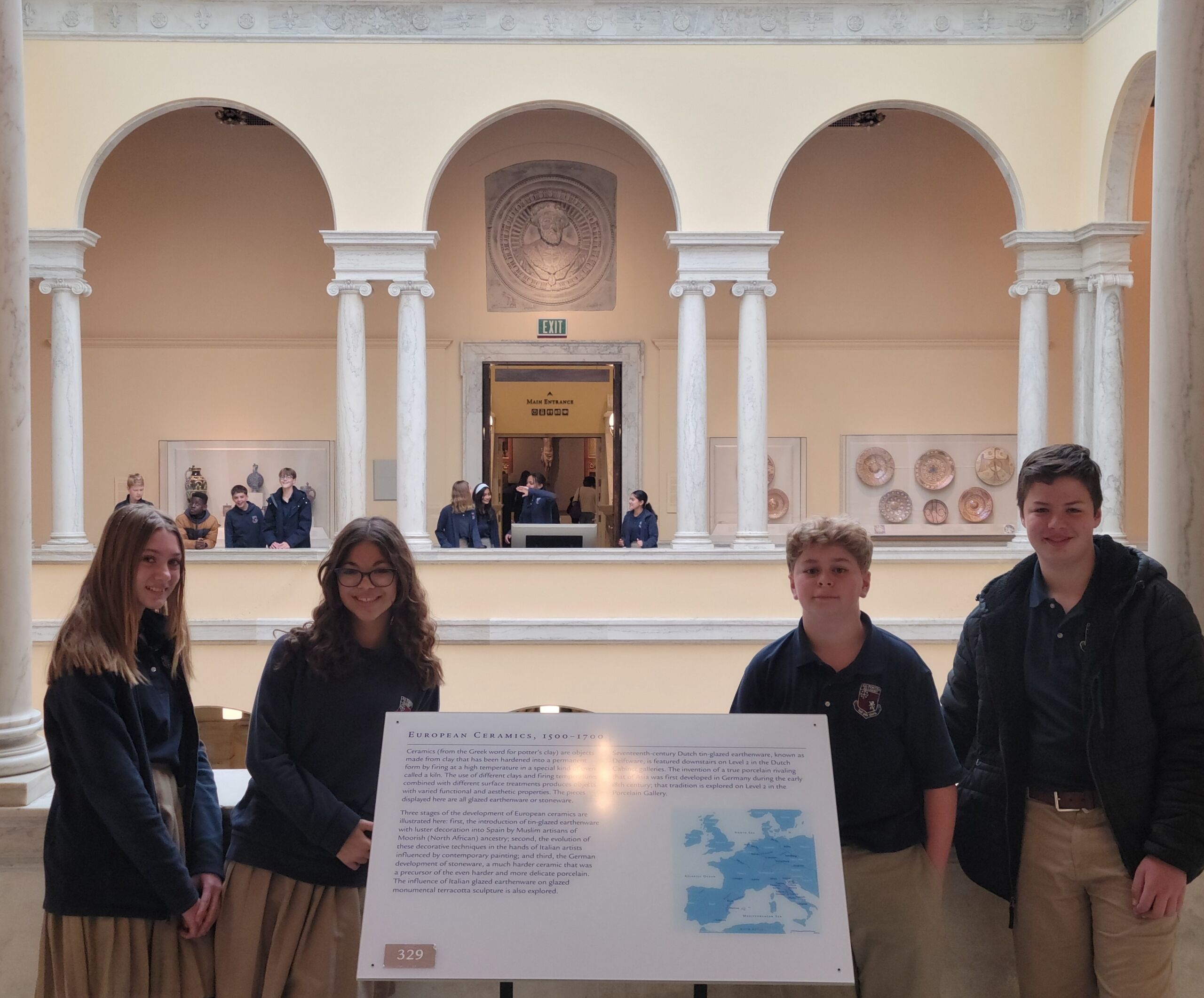 Four Upper Campus students beside an exhibit sign in a museum gallery on a field trip